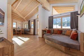 Un interior moderno con techo de madera, un sofá con cojines, zona de comedor y ventanas amplias.
