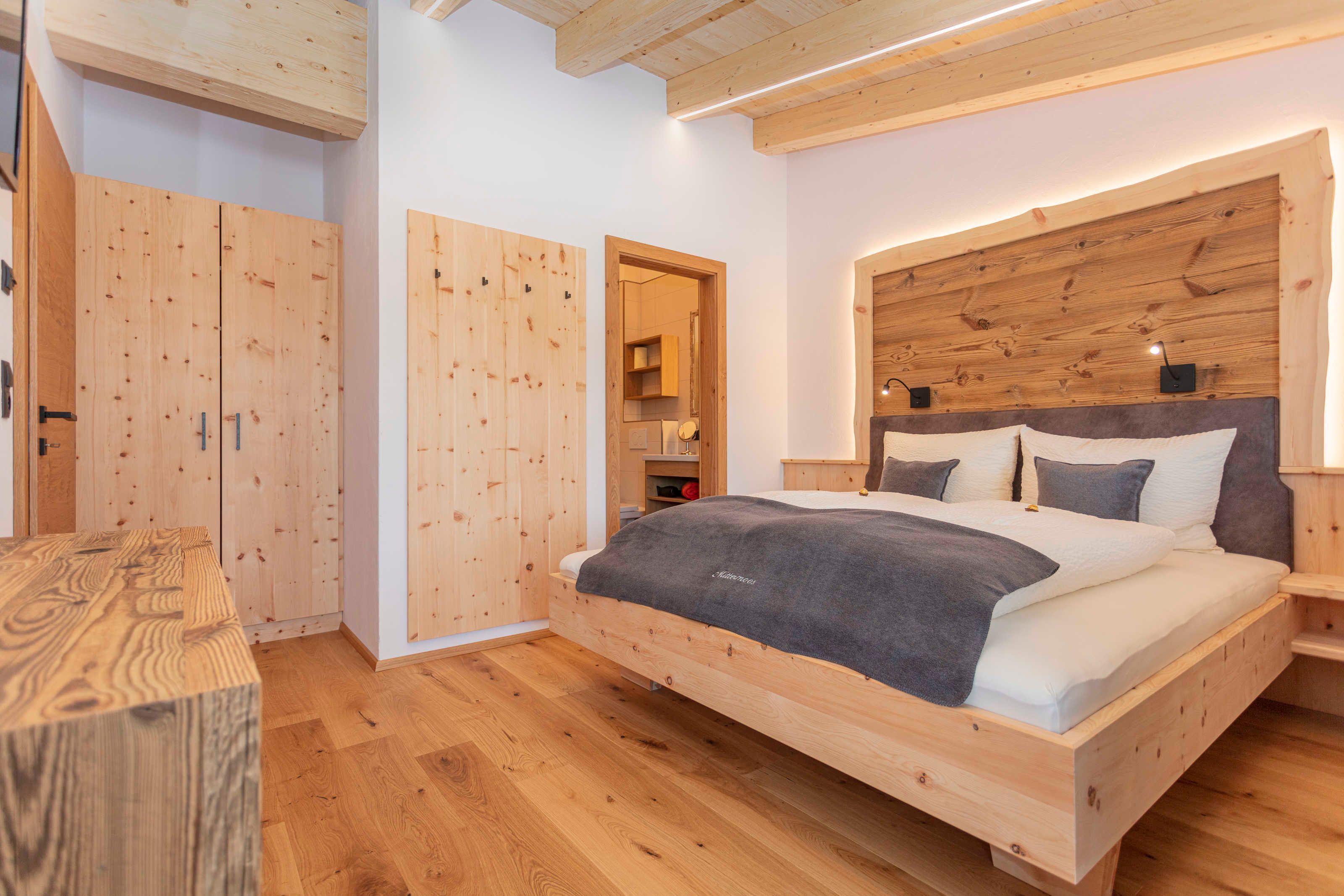 A wooden bedroom with a bed, wardrobe, and a small table.