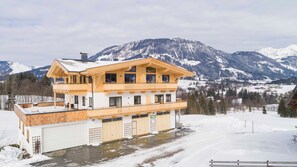 Ein mehrstöckiges Holzgebäude mit Balkonen, einer Garage und Blick auf schneebedeckte Berge.
