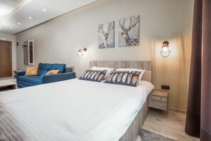 Ein modernes Schlafzimmer mit einem großen Bett, einem blauen Sofa, zwei Wandleuchten und zwei Bildern von Hirschen.