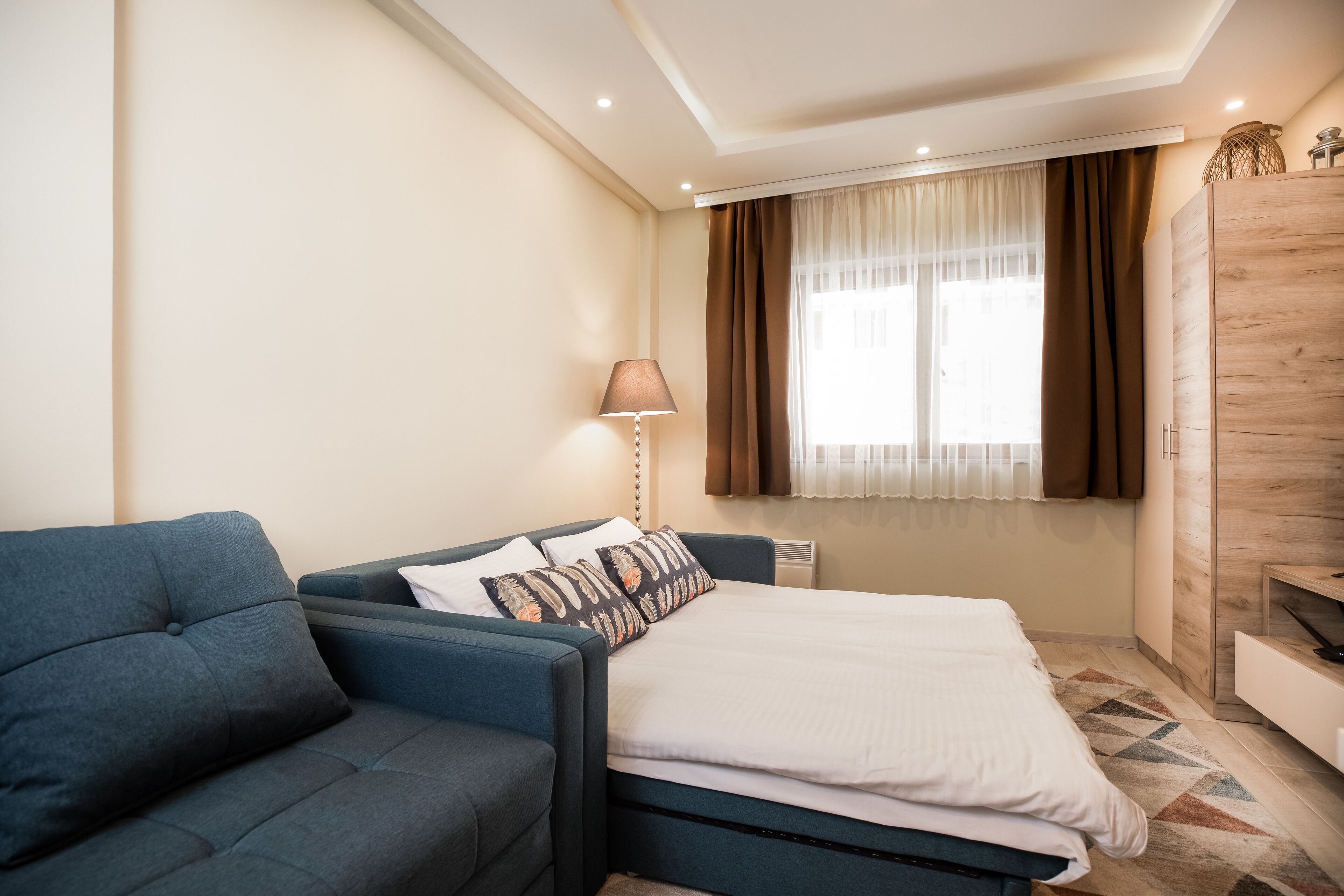 A modern bedroom with a bed, a sofa, a lamp, and a window with curtains.