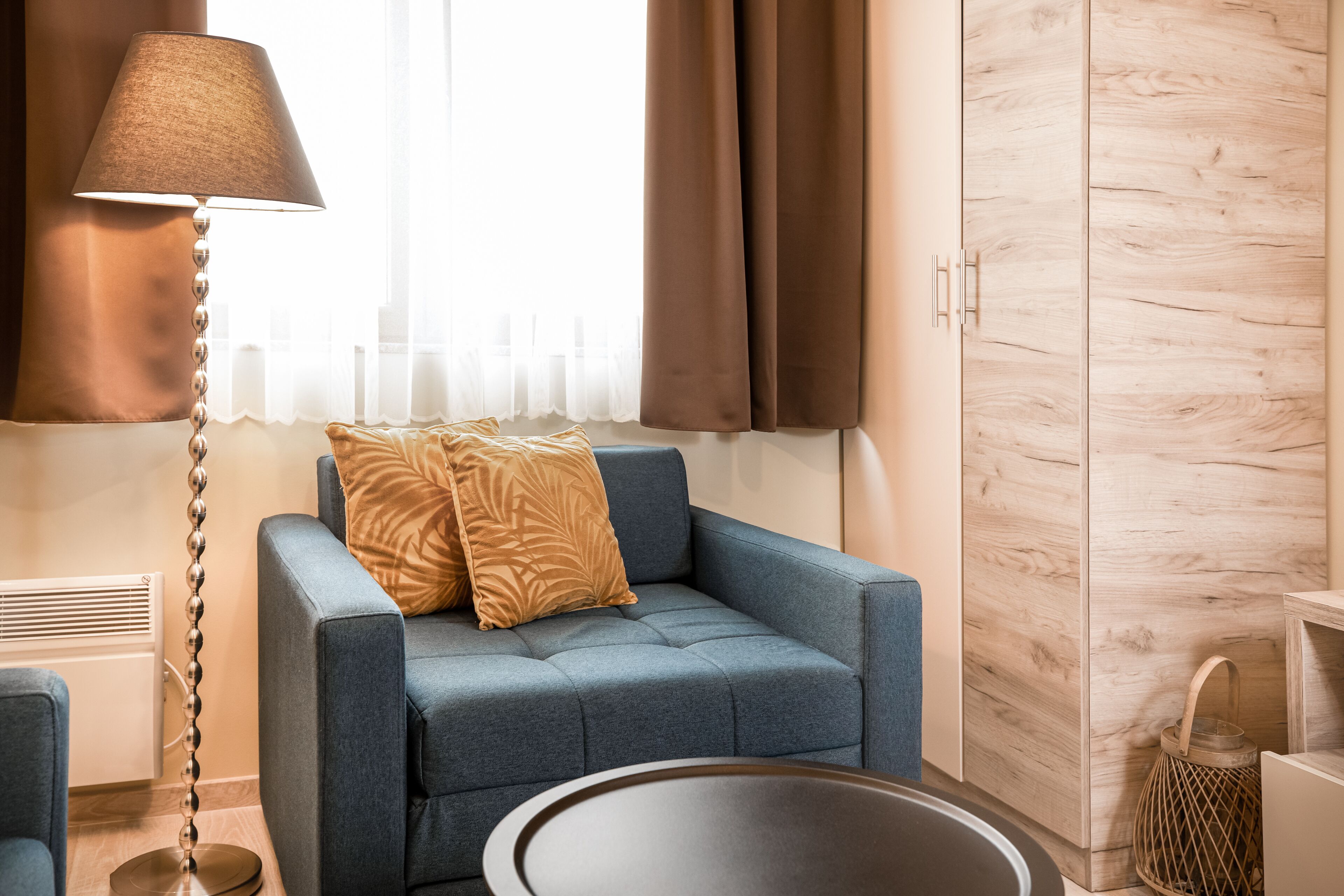 A modern living room with a blue sofa, a floor lamp, and a wooden wardrobe.
