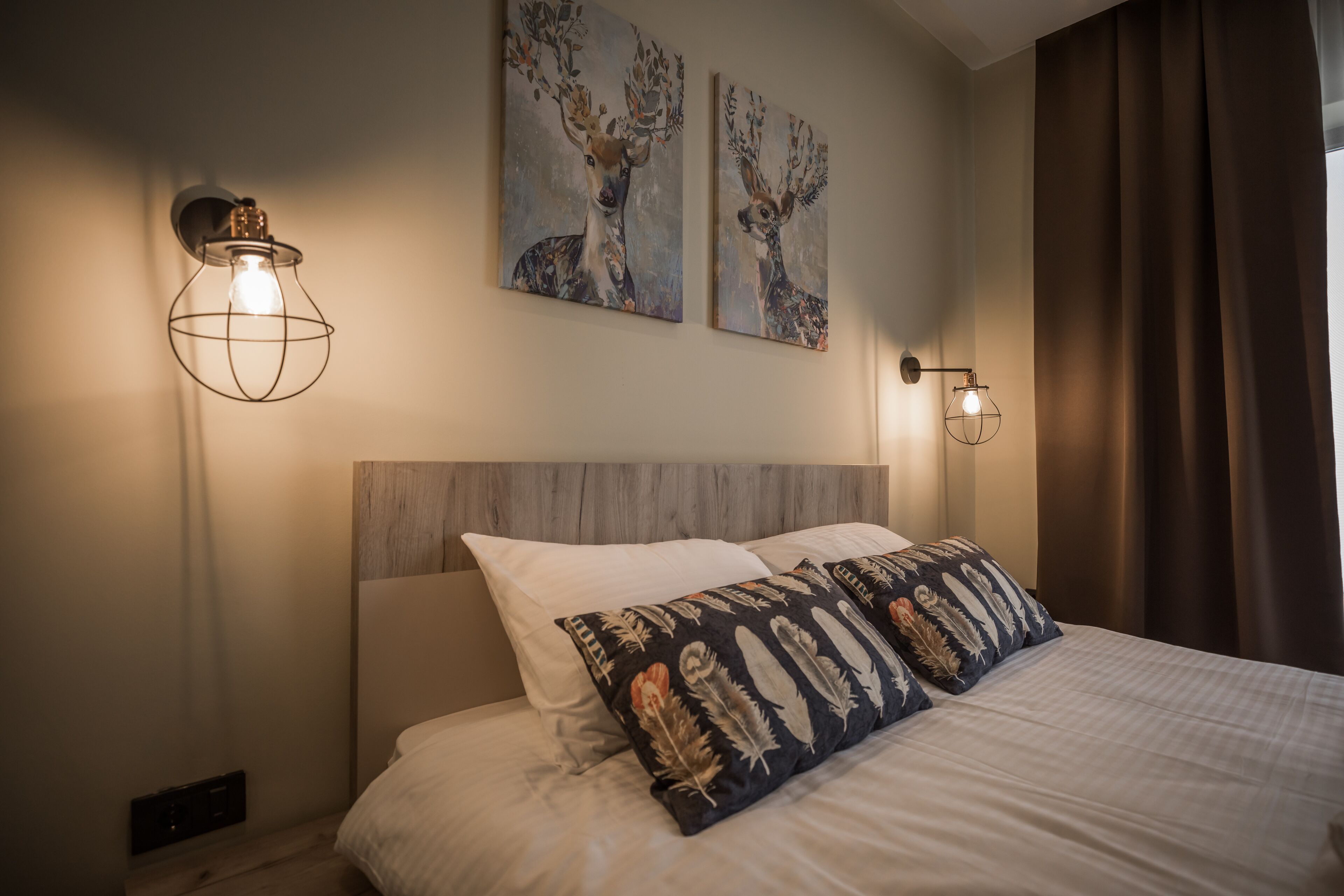 A bedroom with a bed, two wall-mounted light fixtures, and two wall art pieces depicting deer.