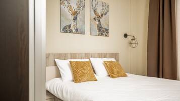 A neatly made bed with white and gold pillows, two wall-mounted paintings of deer, and a bedside lamp.