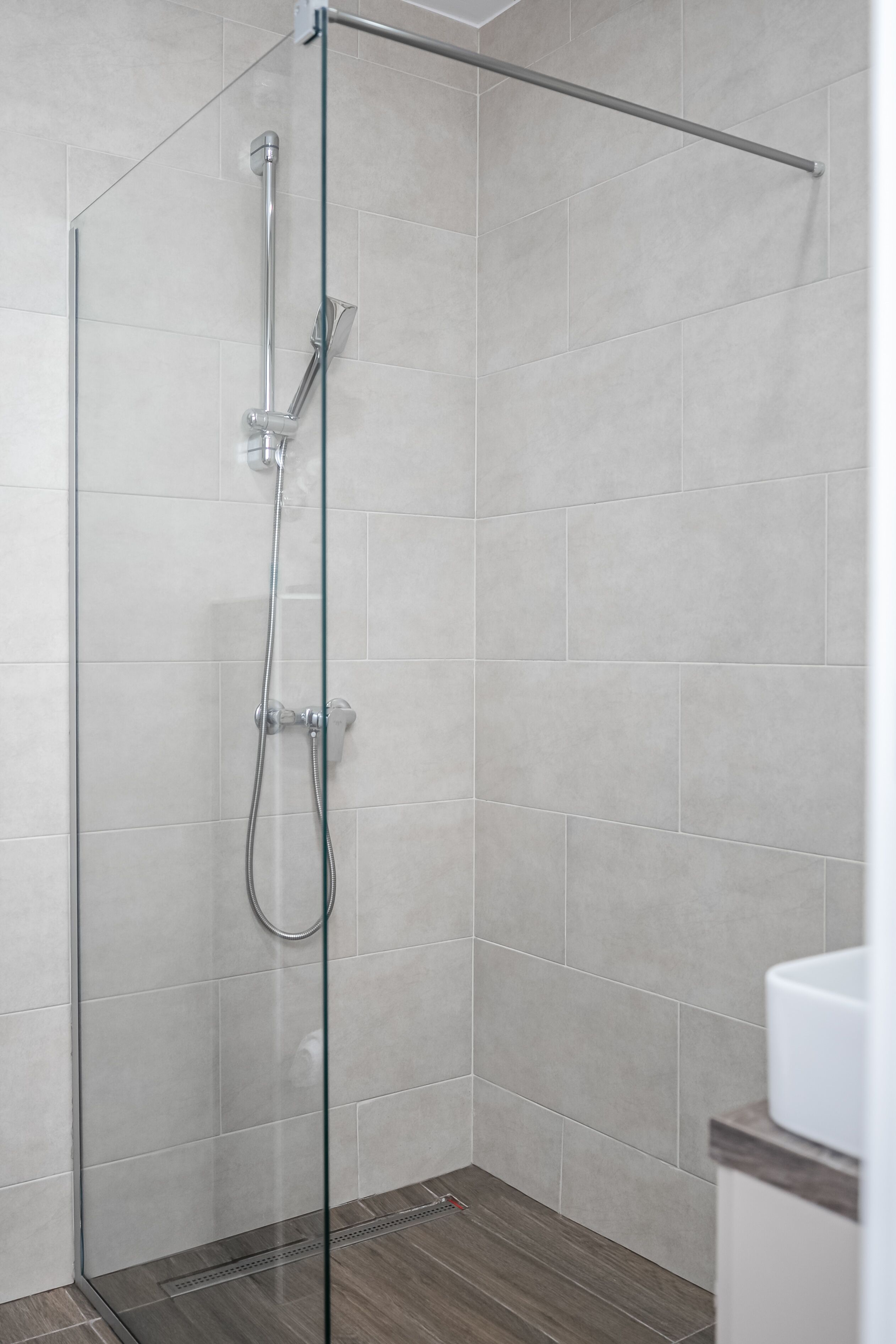 Une douche moderne avec une porte en verre, des murs carrelés et un plancher en bois.