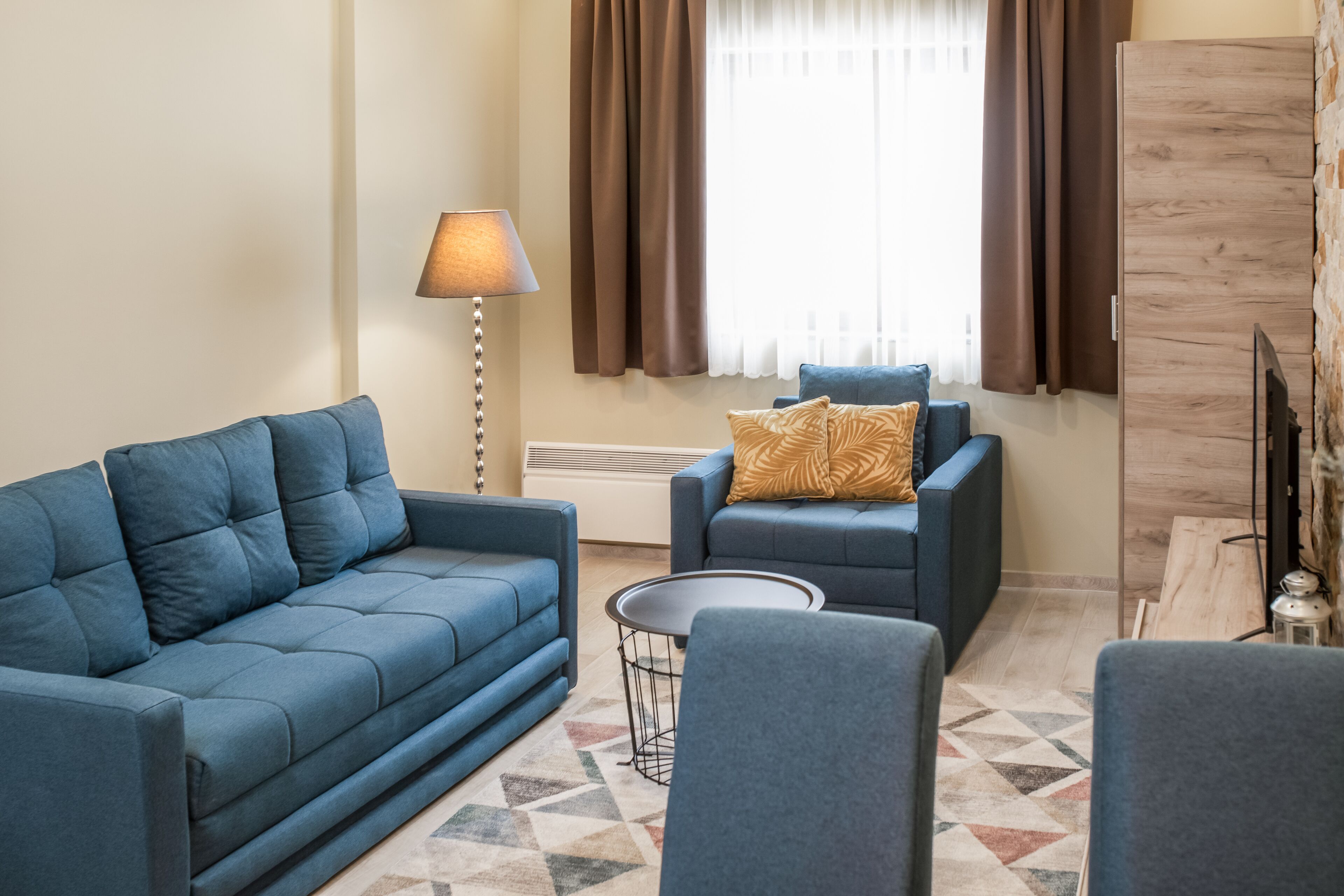 A living room with a blue sofa, a smaller blue armchair, a round coffee table, and a lamp.