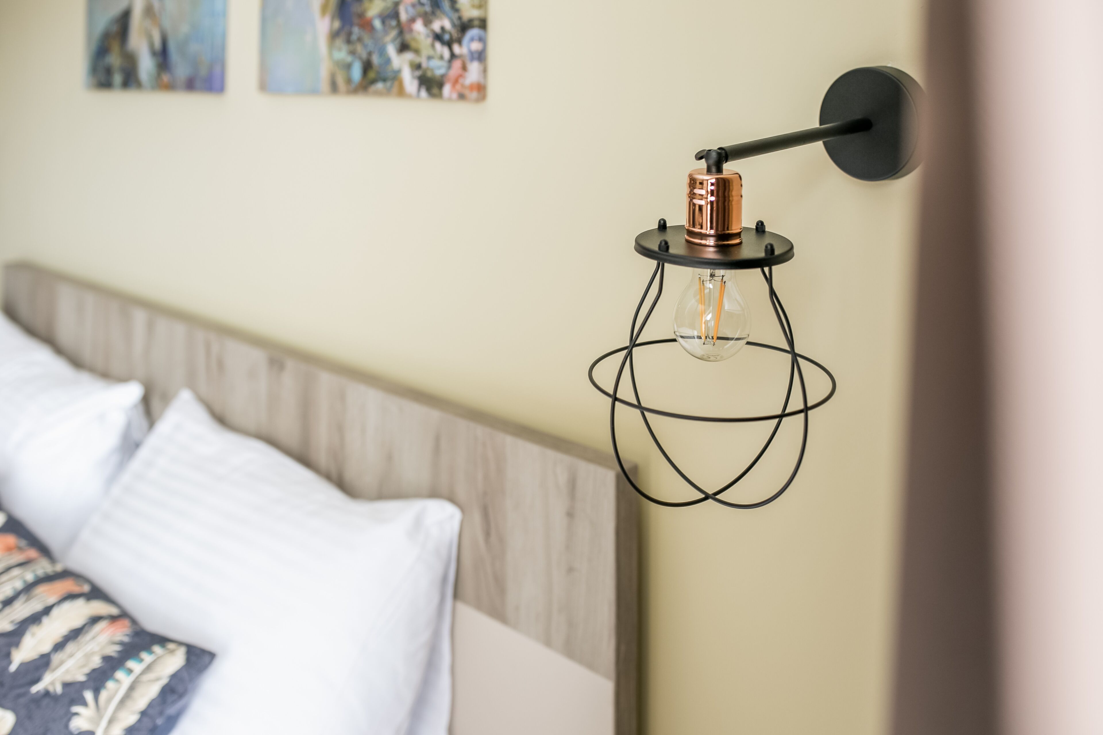 A bed with white and patterned pillows, a wooden headboard, and a wall-mounted light fixture with a clear bulb.