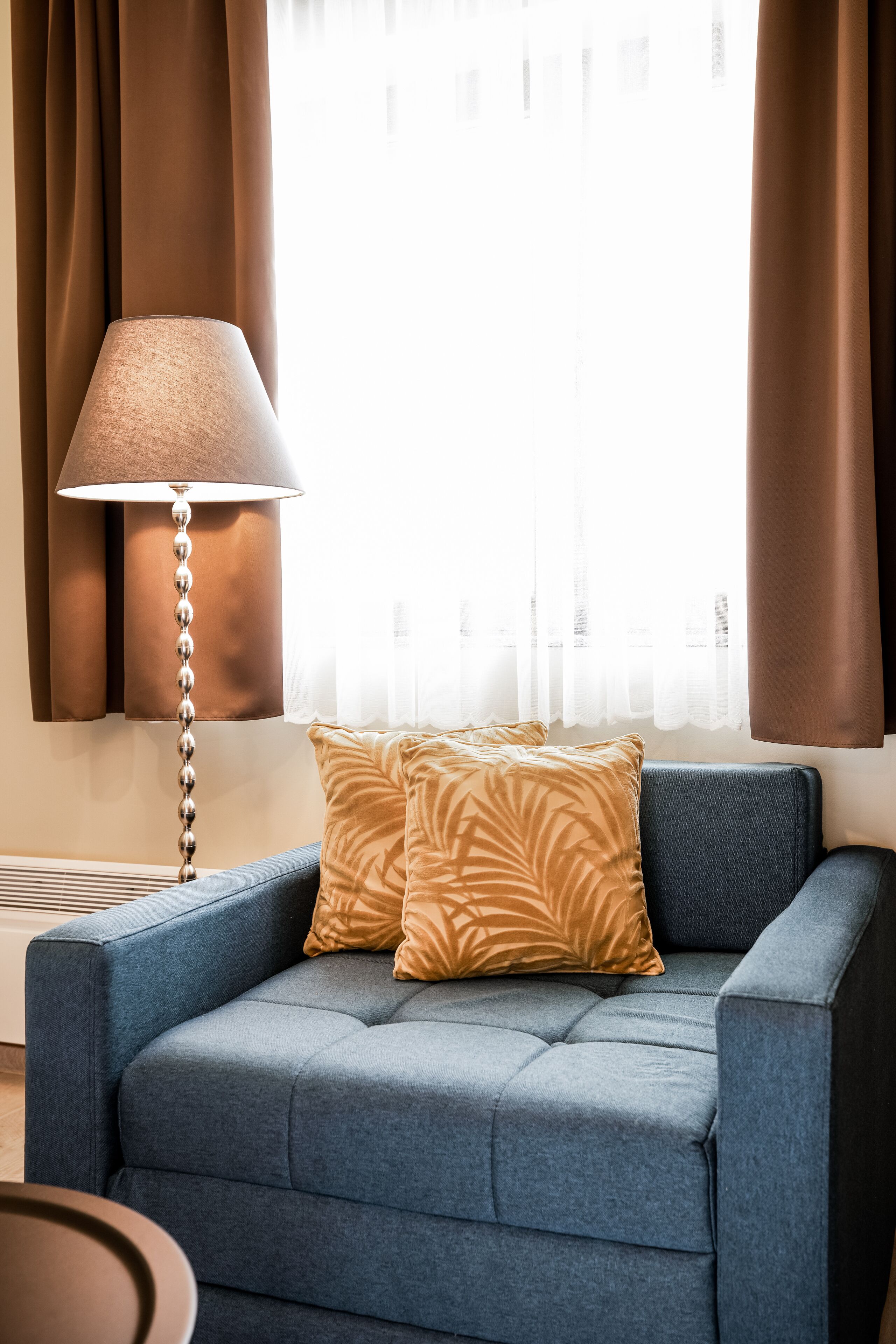 Una sala de estar moderna con un sofá azul, un cojín estampado, una lámpara de pie y una ventana con cortinas.