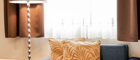Una sala de estar moderna con un sofá azul, un cojín estampado, una lámpara de pie y una ventana con cortinas.