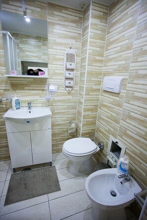 A bathroom with a white sink, toilet, and bidet, tiled in a light wood pattern.