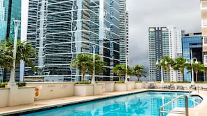 A swimming pool with a view of tall modern buildings, palm trees, and a cloudy sky. - Star Stay Miami / Orange@Brickell - King bed, Balcony & Free Parking (Miami)