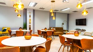 A modern conference room with round tables, orange chairs, and pendant lighting. - Star Stay Miami / Orange@Brickell - King bed, Balcony & Free Parking (Miami)