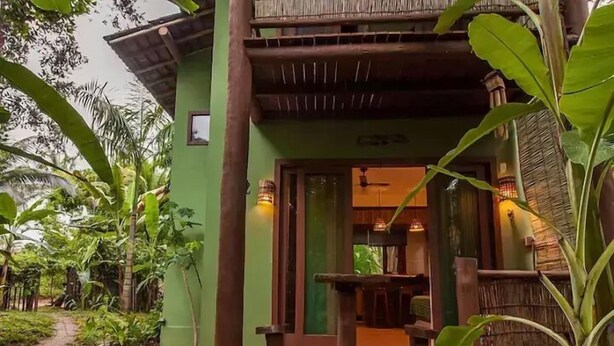 Un terrazza in legno con tavolo e sedie, immersa nel verde e affiancata da un edificio con facciata verde.