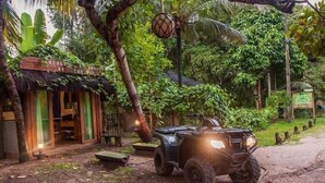 Un edificio rustico con tetto di paglia, un sentiero sterrato e un quadriciclo parcheggiato davanti.