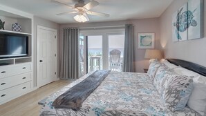 A bedroom with a bed, a TV, a ceiling fan, and a balcony with curtains. - Walton Dunes 7,  Beachfront, Private Beach.  2 Chair/1 Umbrella Set up Included. (Santa Rosa Beach)