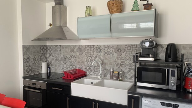 Una cocina moderna con extractor de acero inoxidable, horno microondas integrado, cafetera y lavadora.