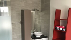 Un baño moderno con cabina de ducha de vidrio, un tocador blanco con lavamanos y una estantería roja.