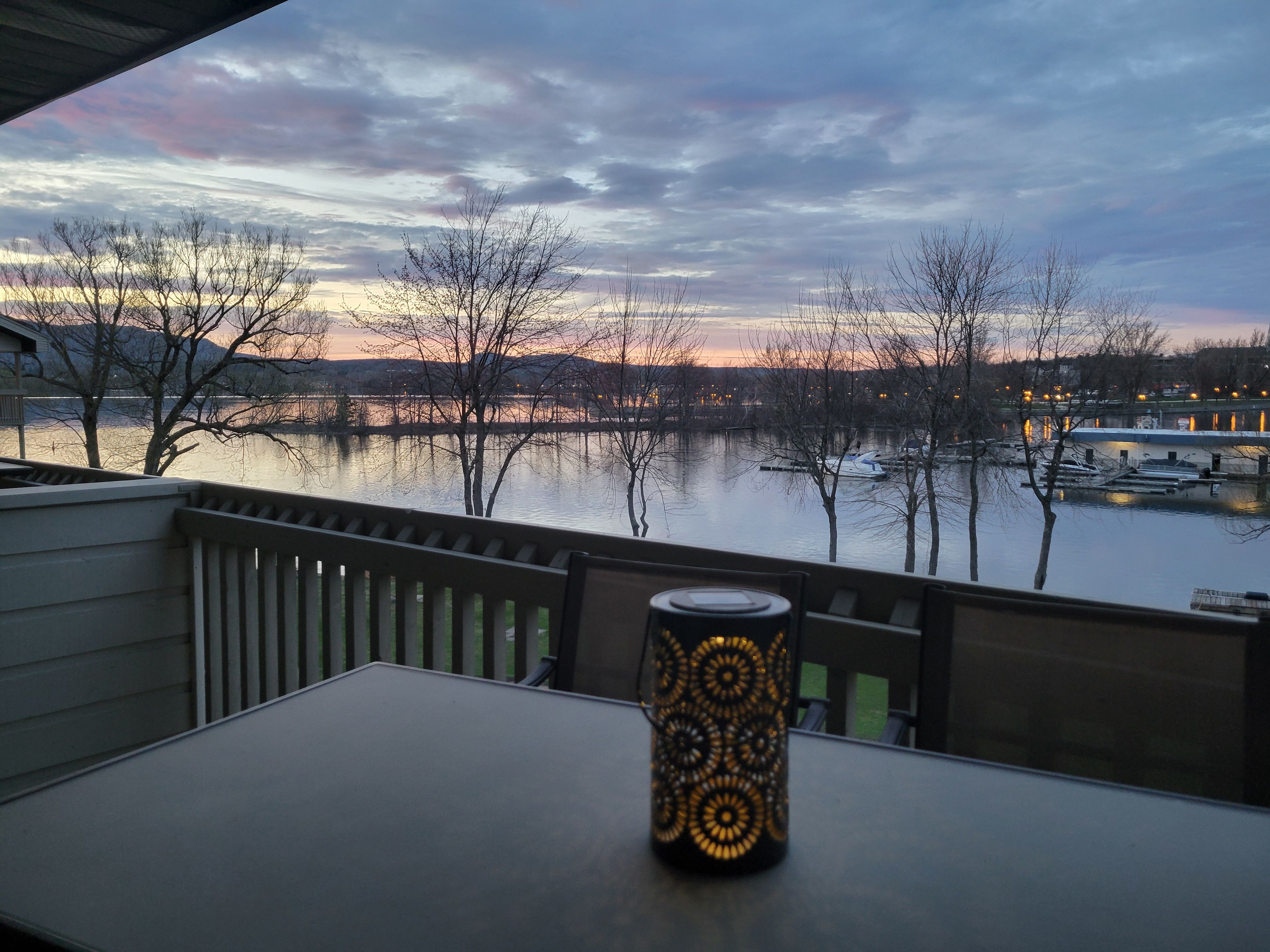 Une table agrémentée d’un porte-bougie décoratif, placée sur un balcon donnant sur un lac où l’on aperçoit des bateaux et des arbres.