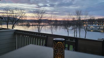 Une table agrémentée d’un porte-bougie décoratif, placée sur un balcon donnant sur un lac où l’on aperçoit des bateaux et des arbres.