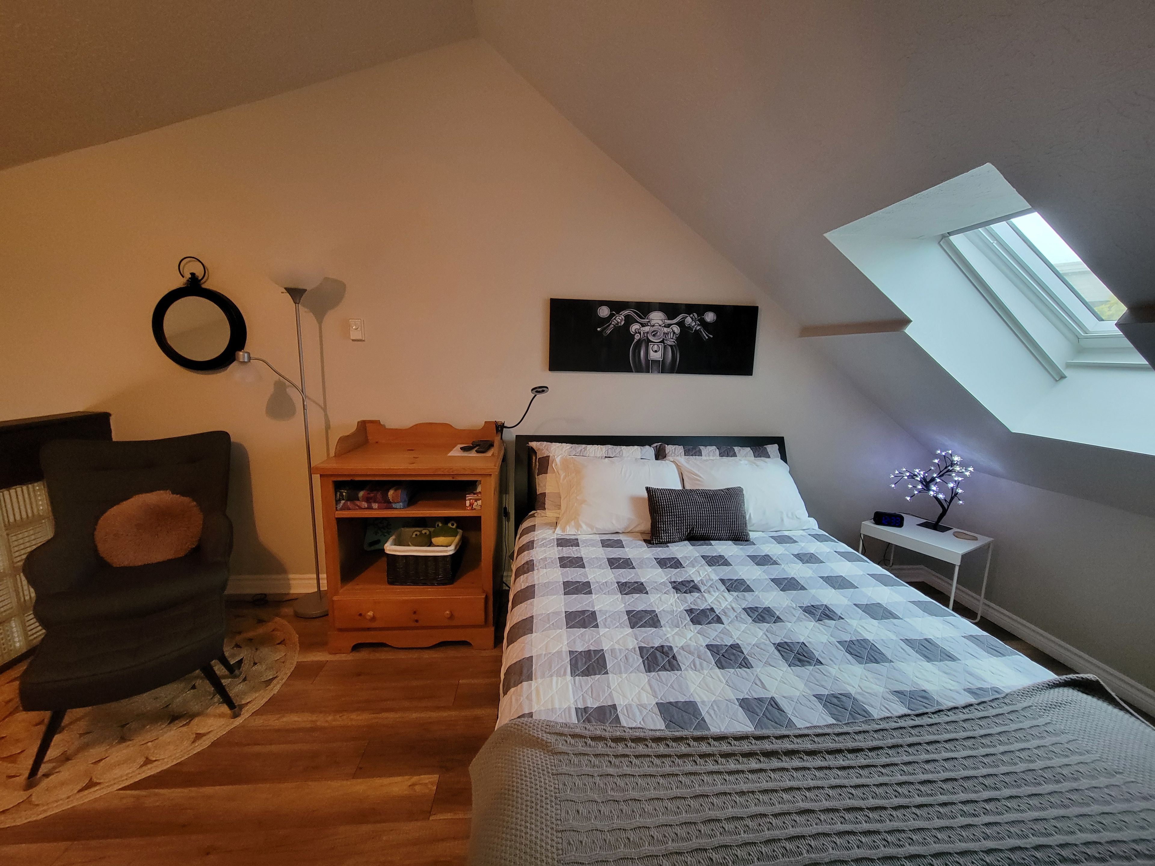 A bedroom with a bed, a chair, a desk, a lamp, and a skylight.
