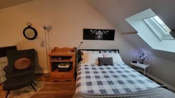 A bedroom with a bed, a chair, a desk, a lamp, and a skylight.