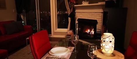 A cozy living room with a fireplace, a dining table set for two, and a red sofa.