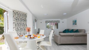A modern dining area with a round table, white chairs, and a beige sofa. - Lamorna, Tregenna Estate, St Ives – Sleeps 4 – On-Site Parking for One Car (St Ives)