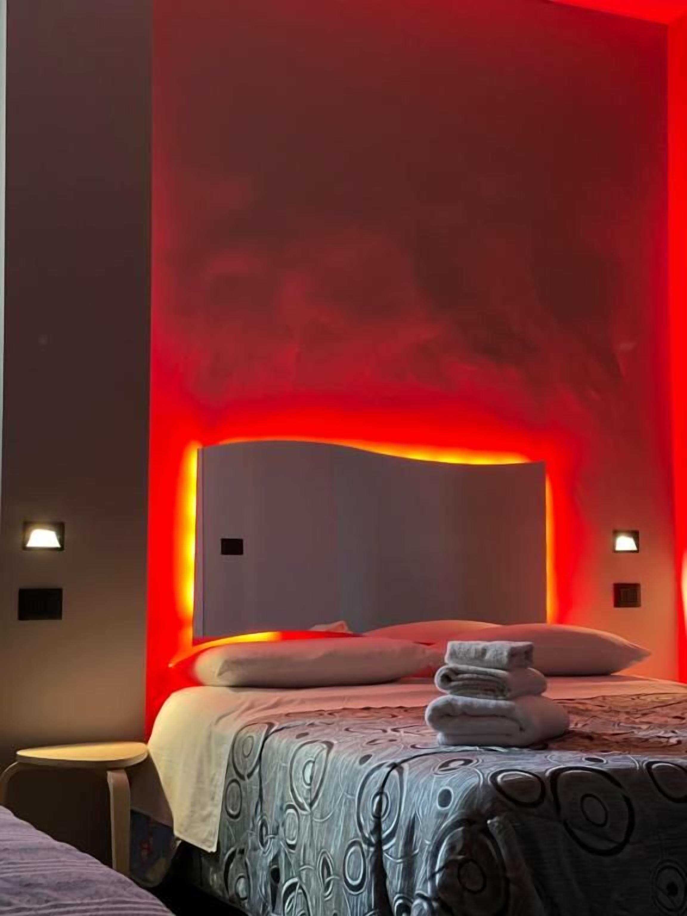 Una camera d'albergo con un letto, un comodino e una lampada a parete.