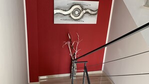 A staircase with a red wall, a modern art piece, and a decorative branch. - The Lux (Adrano)