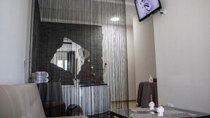 A modern room with a sofa, a glass table with candles, and a TV mounted on the wall. - The Lux (Adrano)
