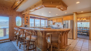 A spacious kitchen with wooden cabinetry, a large island with bar stools, and a view of the mountains. - Valley View Cabin,Lake view, 6 bedrooms, Hot tub, walk distance to village (Big Bear Lake)