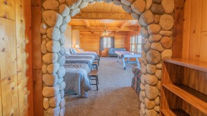 A log cabin interior with a stone archway leading to a room with multiple beds, a pool table, and a wooden ceiling. - Valley View Cabin,Lake view, 6 bedrooms, Hot tub, walk distance to village (Big Bear Lake)