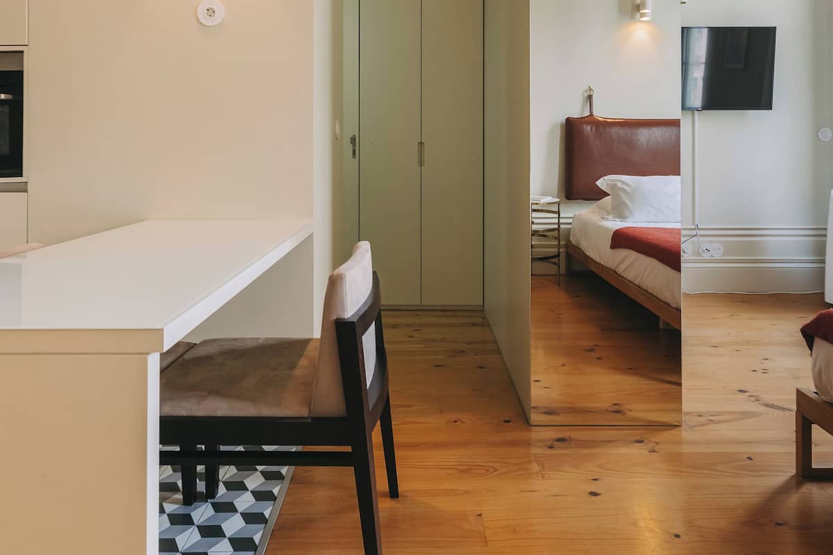 A modern hotel room with a wooden floor, a bed with a red headboard, a desk with a chair, and a TV mounted on the wall.