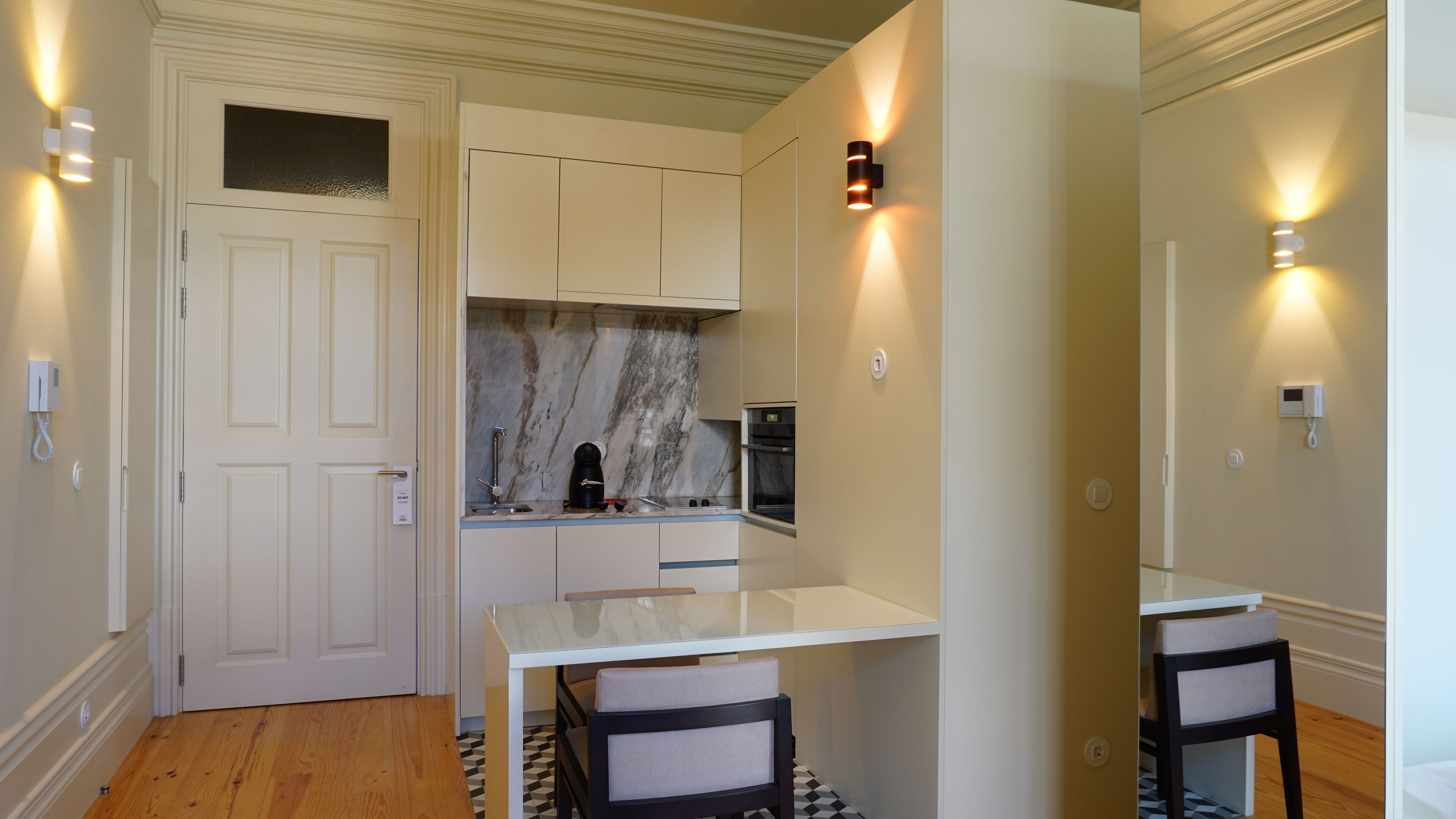 A compact kitchen with white cabinetry, a marble backsplash, and a small dining table with two chairs.