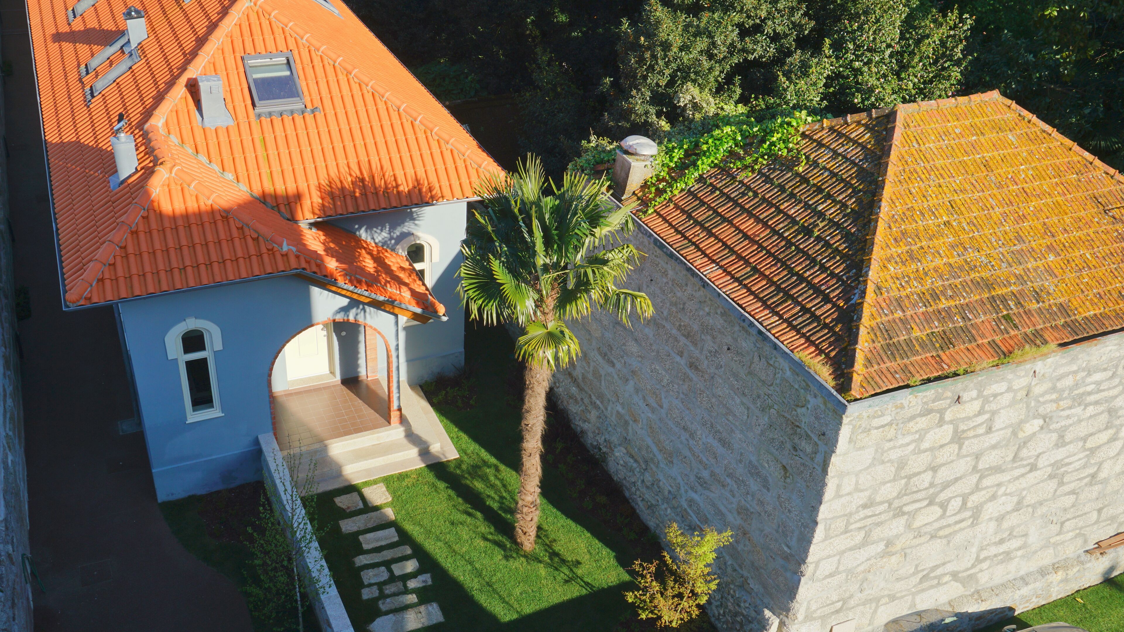 Una casa de dos pisos con techo de tejas, un pequeño jardín y una palmera.