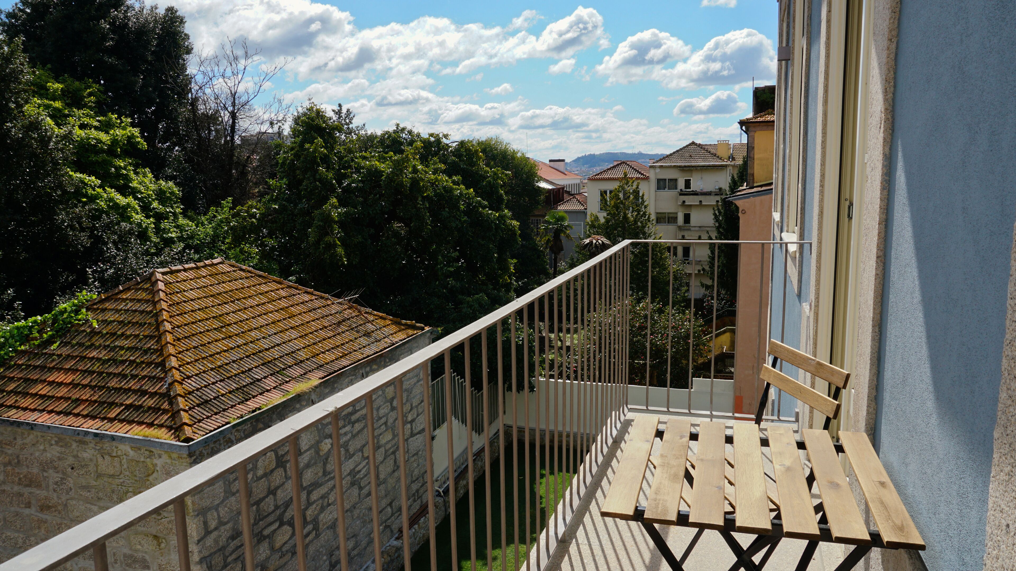 Een balkon met een stenen muur, een houten hekwerk en uitzicht op een woongebied met huizen en bomen.