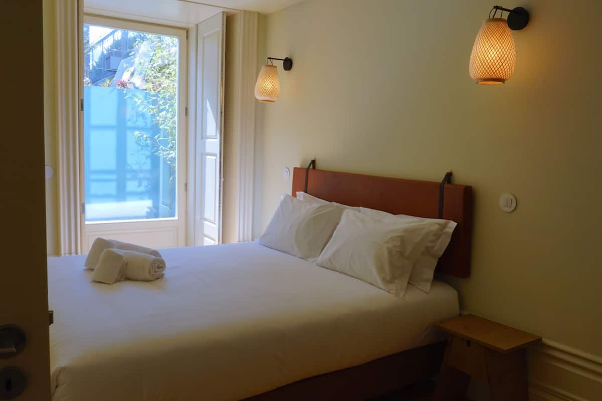 A neatly made bed with white linens and pillows, a wooden nightstand, and two wall-mounted lamps.