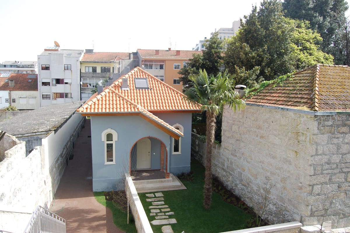A small building with a tiled roof, a stone wall, and a narrow pathway leading to the entrance.