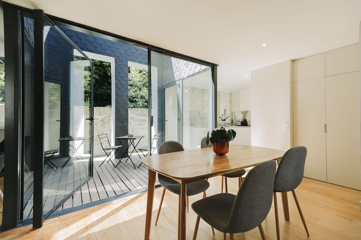 A modern dining area with a wooden table and chairs, a potted plant, and a glass door leading to an outdoor deck.