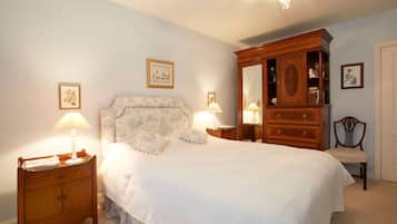 A bedroom with a large bed, two bedside tables with lamps, a wooden dresser, and a chair.