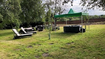An outdoor area with lounge chairs, a small table, a green tent, and a potted plant.