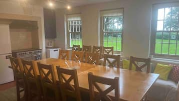 Une cuisine spacieuse avec une grande table à manger et des chaises, un four encastré et une vue sur une pelouse verdoyante grâce à de grandes fenêtres.