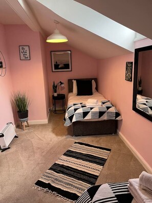 Une chambre à coucher comprenant un lit, une table de chevet, une lampe, une plante en pot, un radiateur et un tapis.