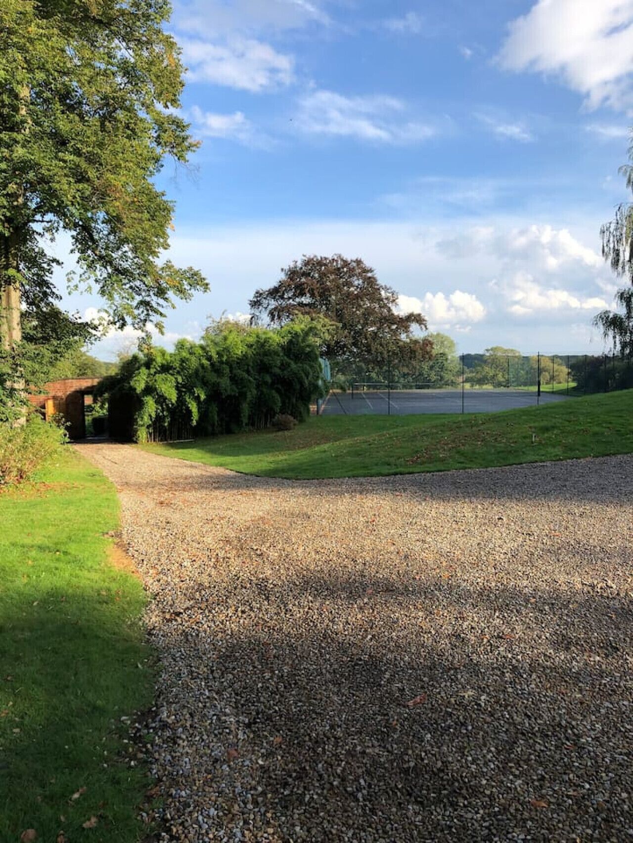 A gravel path leading to a grassy area with trees and a brick structure.