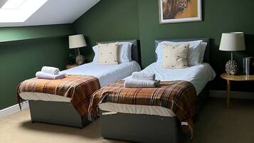 A room with two beds, a skylight, a painting of a yak, and a round table with a lamp.