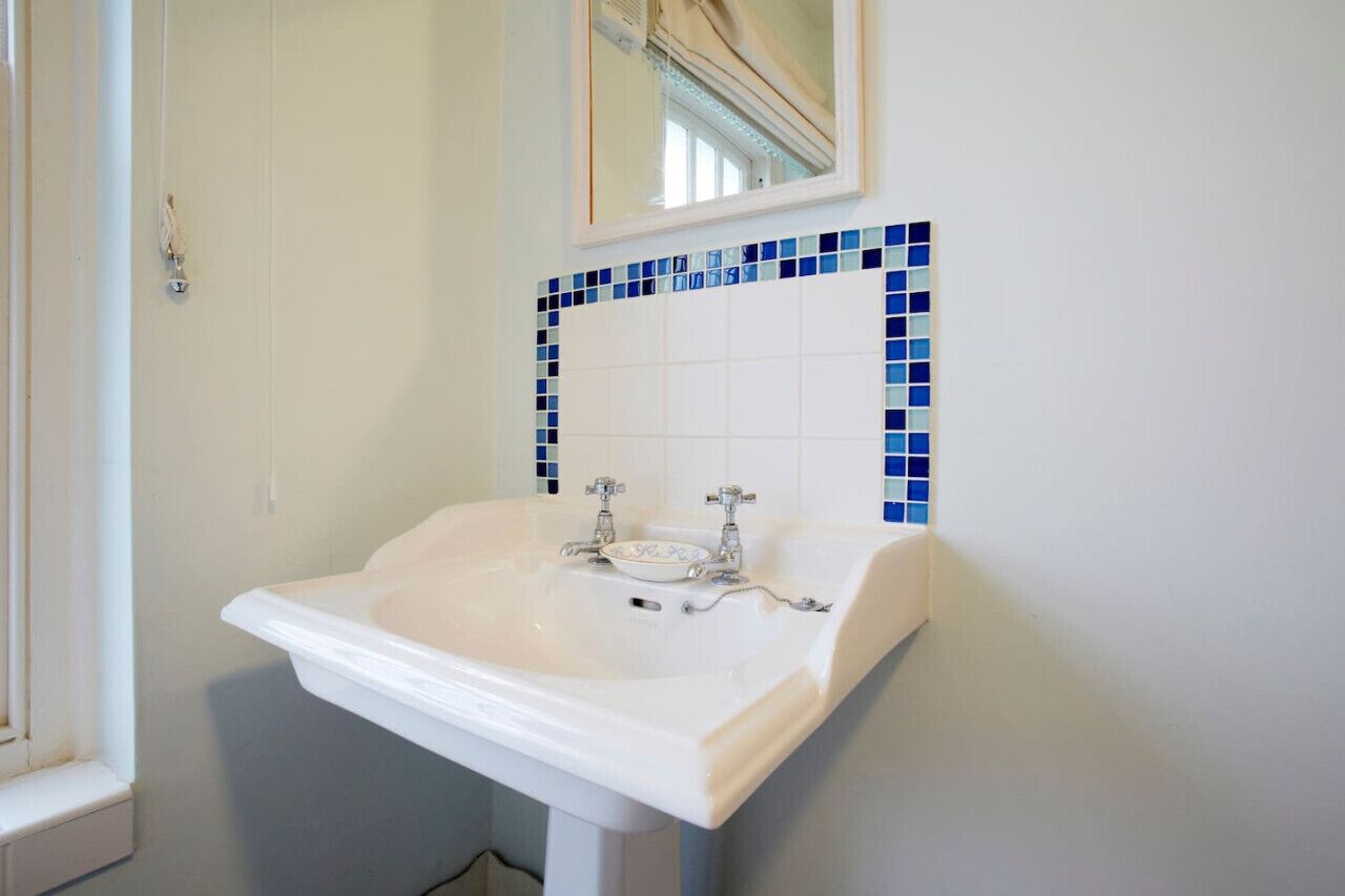 A bathroom with a white sink, blue mosaic tiles, and a mirror above it.
