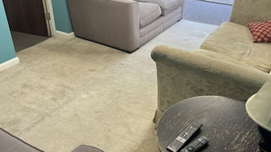 Un soggiorno con un divano color beige, un tavolino con due telecomandi e vista su una zona patio esterna.