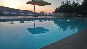 En swimmingpool med liggestole og en parasol, omgivet af en stenvæg og træer.