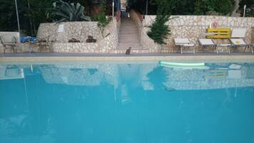 Una piscina con un muro de piedra y escalones que suben a una terraza de madera.