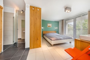 A modern bedroom with a bed, a wooden wardrobe, a bathroom with a glass door, and a large window with curtains.